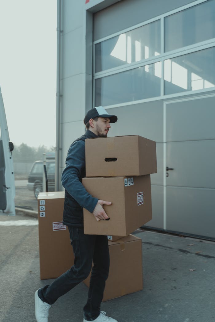A delivery man carrying cardboard boxes to a loading dock outside an industrial building.